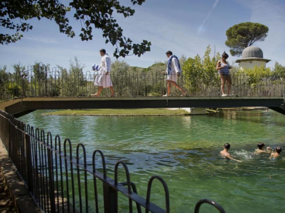 Unos bañistas pasan sobre el puente del lago de un balneario de Alhama de Aragón