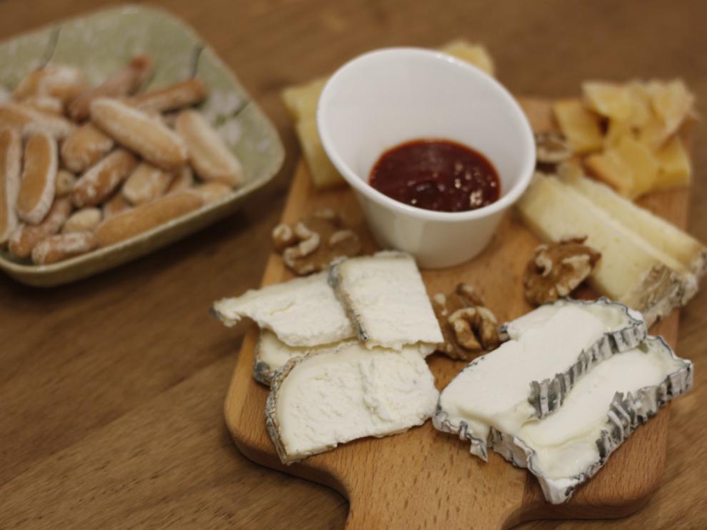 Una tabla de quesos con cinco variedades acompañada de mermelada de pimiento, nueces y picos de pan.