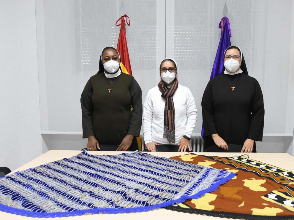 Las hermanas franciscanas Clara Natalia Vera (izquierda), Claudia Sofía Cortés (centro) y Janeth Aguirre posan junto a los mantos confeccionados por mujeres de Mali para la Virgen del Pilar, en el Acuartelamiento San Fernando en Zaragoza.