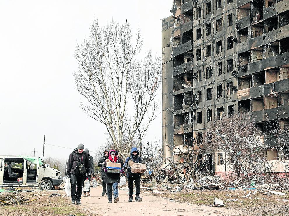 ​Varias personas caminan en Mariúpol junto a un edificio destrozado por las fuerzas rusas