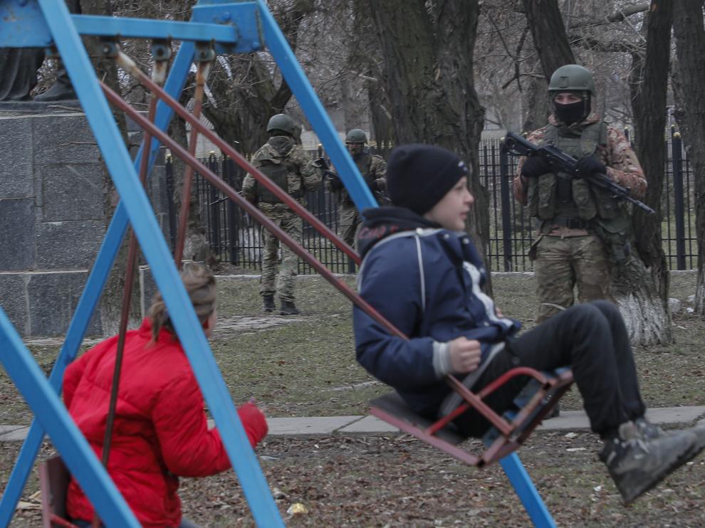 Niños ucranianos en un parque ante la mirada de un soldado ruso en en Lugansk.