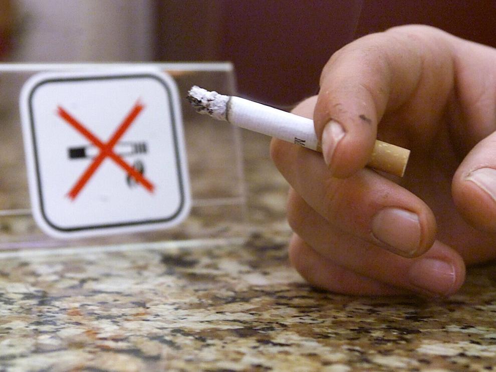 Un fumador, junto a un cartel de prohibido fumar.