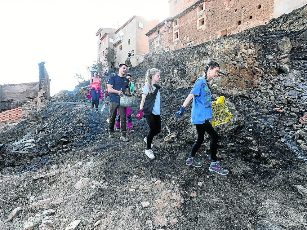 Un grupo de jóvenes limpian la zona quemada en Moros, que llegó a las puertas de los locales de las peñas.