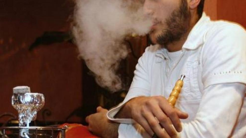 Un joven fuma tabaco con una cachimba en un café de París.
