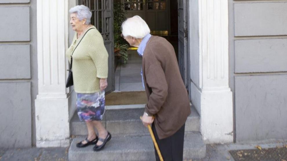 Dos personas mayores, delante de un portal donde se venden pisos.