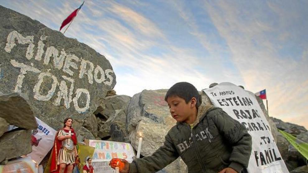 Un niño enciende una vela en un altar del campamento de la mina San José (Chile), ayer.
