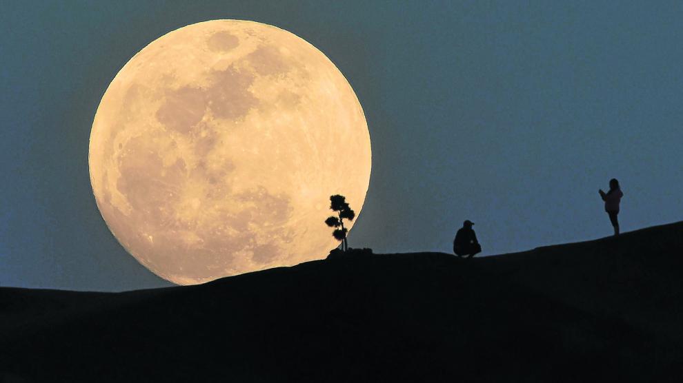 A person poses for a photo as the moon rises over Griffith Park in Lo