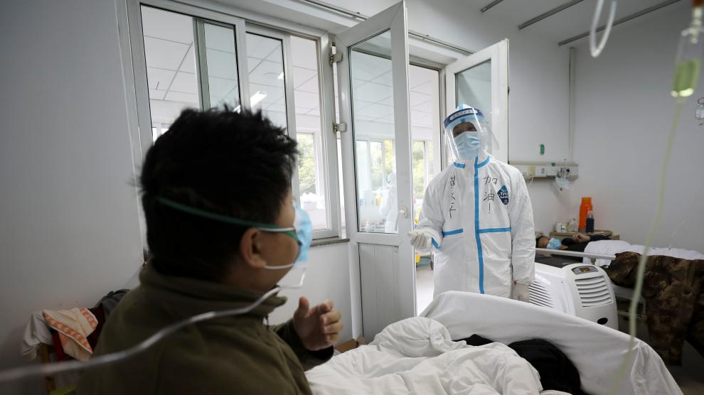Un profesional sanitario con el traje de seguridad interactúa con un paciente en una habitación de aislamiento de un hospital en Wuhan.