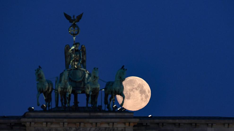 An almost full moon is seen behind the quadriga of Brandenburg Gate in Berlin