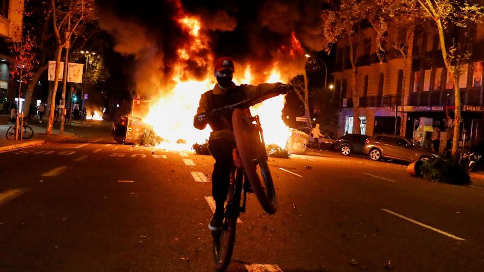 Un joven con una moto pasa junto a una barricada ardiendo en Barcelona