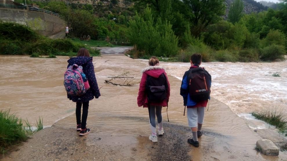 Varios escolares observan el vado de acceso a Los Ramones, intransitable por la crecida del Mijares.