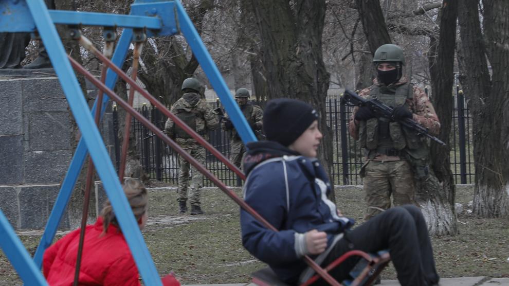 Niños ucranianos en un parque ante la mirada de un soldado ruso en en Lugansk.