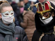 Dos personas pasean por Venecia con máscaras de carnaval y mascarillas protectoras.