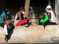 Jóvenes con mascarillas miran sus móviles en una calle de La Habana.