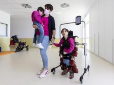 Rebeca Morfioli con sus hijas gemelas Sara (en brazos) y Noa, caminando con el exoesqueleto pediátrico, el miércoles en el Colegio de Educación Especial Atades-San Martín de Porres en Zaragoza.