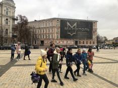 Un grupo de estudiantes se dirigen a la exposición ante un cartel recordando la hazaña de Mariupol