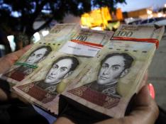 Una mujer sostiene varios billetes de 100 bolívares para cambiarlos.