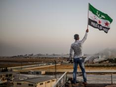 Un ciudadano sirio ondea una bandera del país en la frontera con Turquía