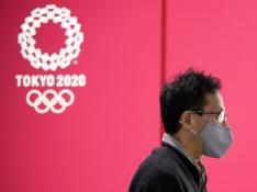 Una persona con mascarilla pasa en Tokio junto a un cartel anunciando los Juegos Olímpicos.