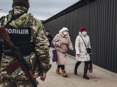 Dos mujeres caminan delante de un policía en el control fronterizo de Stanitsa Luganska para cruzar del territorio ucraniano al territorio de la autoproclamada República de Lugansk