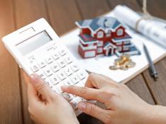 female-hand-operating-calculator-in-front-of-villa-house-model