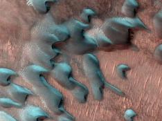 Esta imagen adquirida el 22 de julio de 2022 por el Mars Reconnaissance Orbiter de la NASA muestra dunas de arena moviéndose por el paisaje. La escarcha invernal cubre la mitad más fría de cada duna que mira al norte